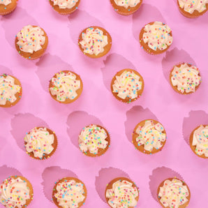 Vegan Vanilla Cupcakes with smooth plant-based icing and rainbow sprinkles on pink background by Crumbs & Doilies